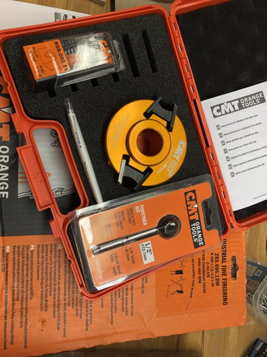 Öppnad verktygsförpackning med CMT Orange routerbits och skärstål för träbearbetning, inklusive skärbits och instruktionsblad.