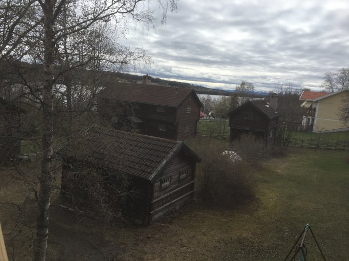 Vy från taket med flera träbyggnader i en gård omgiven av träd och en gräsmatta.