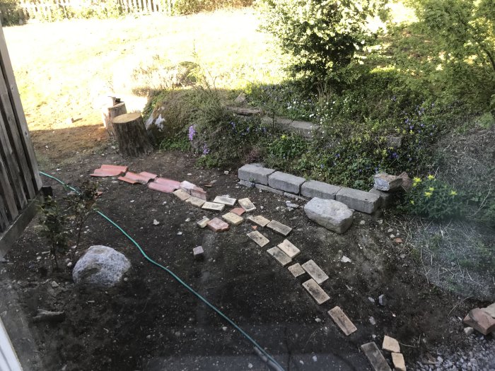 Jordplätt utanför hus med några utspridda stenplattor och tegelstenar som bildar en improviserad gång.