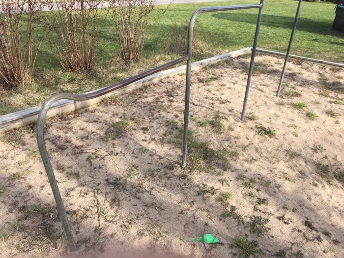 Sned knäveckshängställning i metall på sandmark med gräs och buskar i bakgrunden.