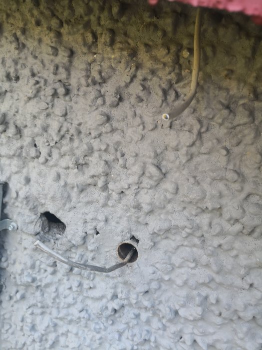 Avklippt kabel som sticker ut från ett hål i en råbetongvägg.