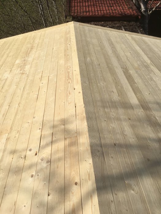 Nyinstallerad råspont på ett tak, redo för papp, med skuggor av träd och del av ett rött tak i bakgrunden.