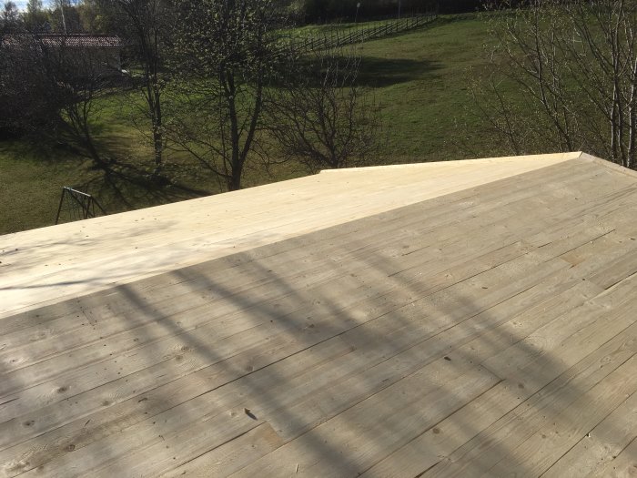 Nybyggt råsponttak med skuggor från träd, klar för nästa steg i byggprojektet.