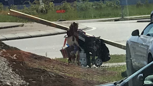 Person som bär en trave brädor medan de går förbi en byggarbetsplats och parkerade bilar.