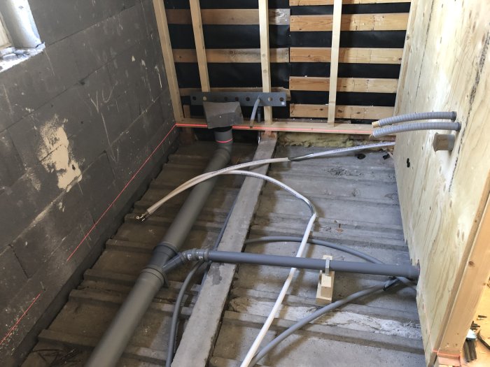Pågående badrumsrenovering i ett hem med synliga rörinstallationer och stödreglar på väggar och golv.