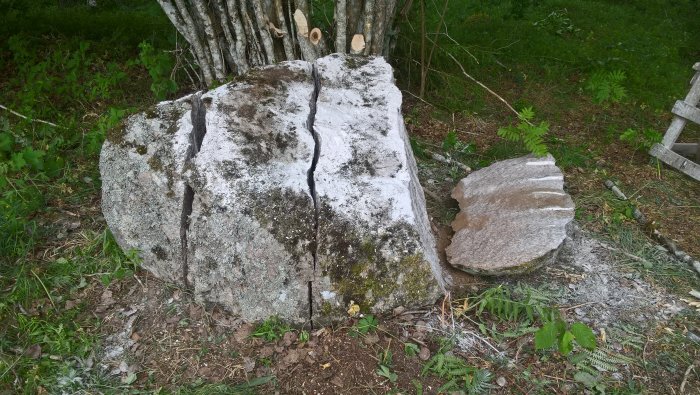 Stor sten kluven i två delar med tydlig spricka, nära träd och grönska, resultat av använd maskin.