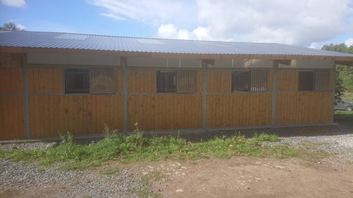 Nybyggt stall med träväggar och flera fönster, beläget i en lantlig miljö under en klar himmel.