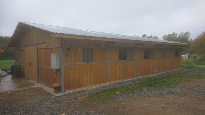 Nybyggt stall med träbeklädnad, flera fönster och ventilationsgaller, befintlig i en lantlig miljö.