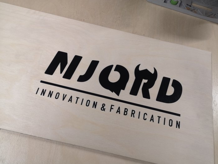 Träplanka med bränt motiv "NJORD INNOVATION & FABRICATION" skapat med vinylplotter och salmiak.