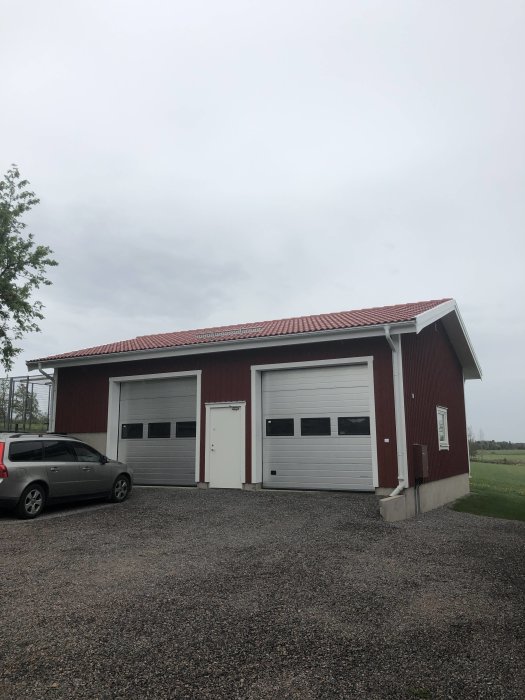 Nybyggd dubbelgarage med röd fasad och vitt garageportar på en grusuppfart.