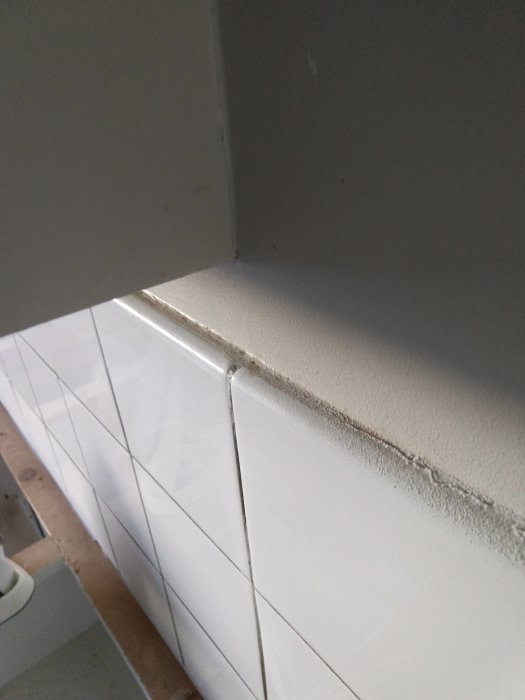 Kökshörna med vit väggkakel som ska tas bort, visar fogar och ineffektiv ytnivå mellan kakel och vägg.