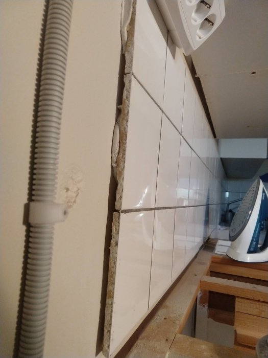 Vit kakelvägg med borttagen platta, exponerad fix och eluttag, under renovering.