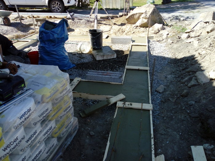 Nyutgjuten kantbalk på grusunderlag med träformar och säckar av byggmaterial i förgrunden.