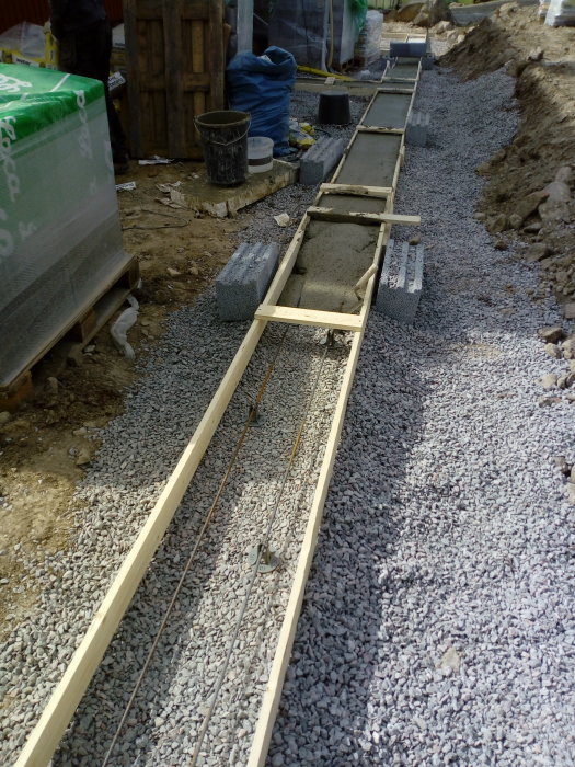 Kantbalk gjuten i betong vid byggarbetsplats, omgiven av grus och byggmaterial.