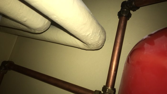 Isolerade vattenrör och ett kopparledningsrör i ett takutrymme.