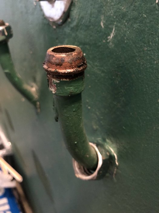 Gammal rörstump med klämringskoppling mot en grön vägg, troligen från 50-talet.