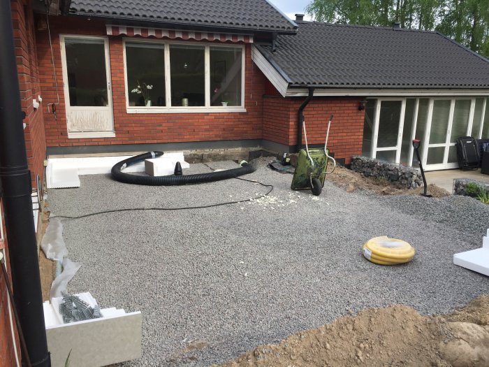 Uppmätt område med kantelement och makadam för grundläggning av uterum intill tegelhus.