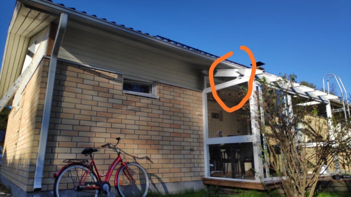 Husfasad med markerad punkt för ventilation, stege, cykel och terrass i förgrunden.