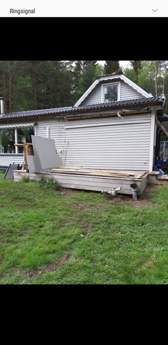 Hus med rivet tak och materialstackar på marken, redo för fasadrenovering.