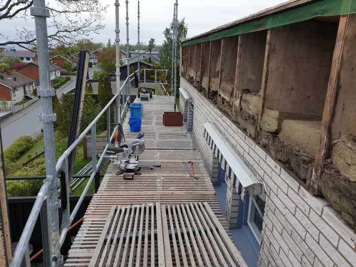 Metabo KGS 216 kap- och geringssåg placerad på en byggplats med träplank och verktyg, utsikt över bostadsområde.