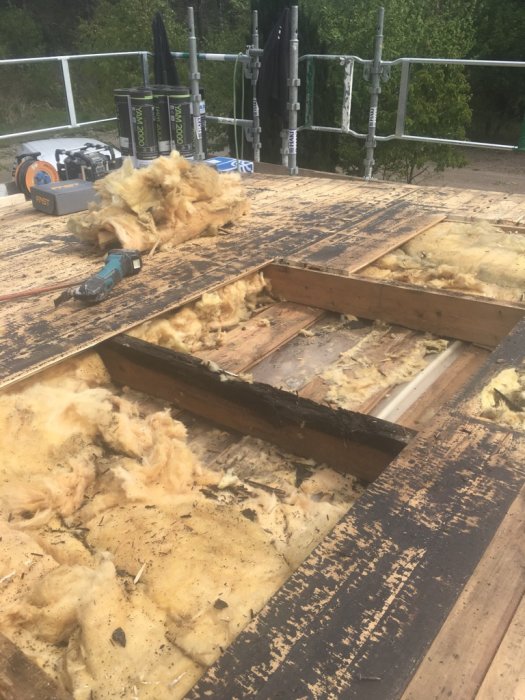 Renoveringsarbete på tak med gammal isolering och verktyg, trasig råspont synlig.