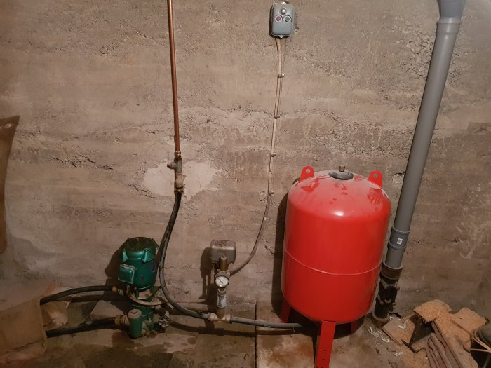 Gammal vattenpump och röd tryckbehållare för trädgårdsbevattning i källare.