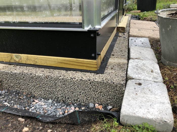 Nybyggt växthusfundament av lecablock, träregel och metallsockel med marksten intill.