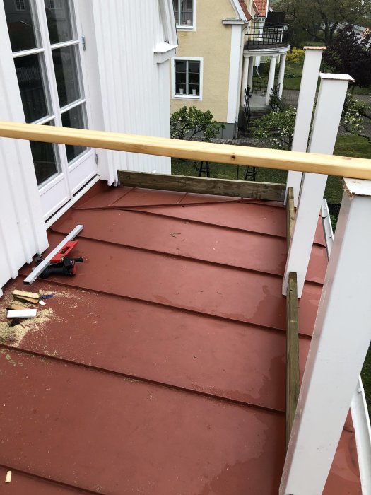 Påbörjat arbete med balkongbygge under regnigt väder med uppsatta vita stolpar och en regelram på en röd trall.
