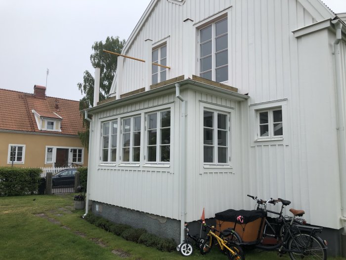 Halvfärdig balkongkonstruktion med uppsatta stolpar och regelram runt en vit husfasad på en regnig dag.