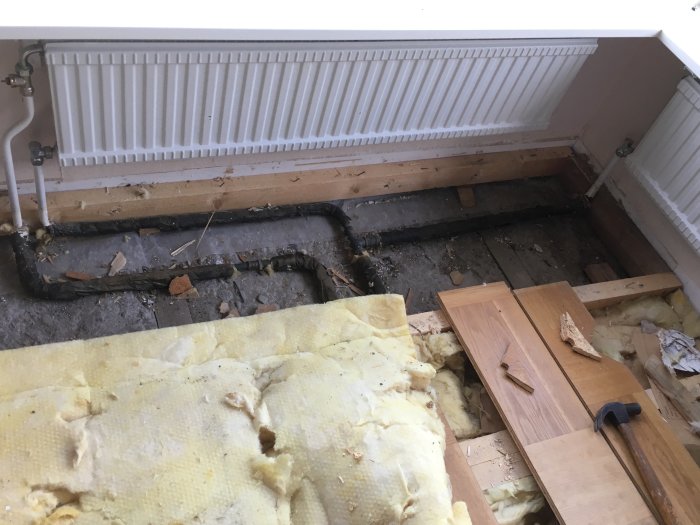 Gamla järnelementrör under renovering av golv i vardagsrum, med upprivet golv och isolering synligt.