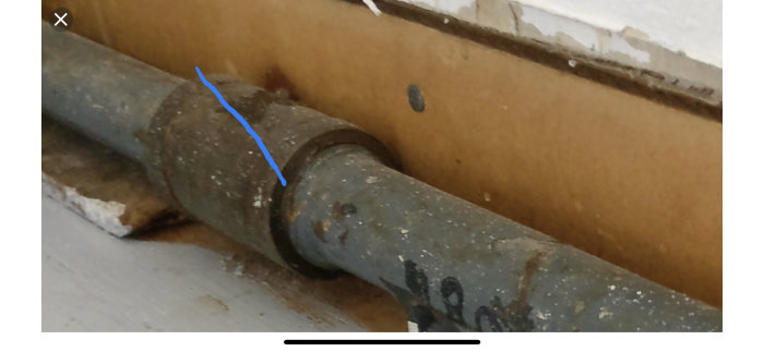 Ett gammalt metallrör med en skarvmuff markerad med en blå linje där sågningen är tänkt att göras.