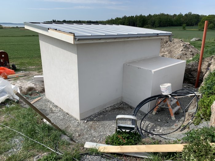 Betongkonstruktion av en matkällare och dagvattenbrunn under arbete, omgivet av kabelrullar och byggmaterial.