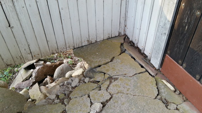 Söndersprucken och skadad betongtrapp vid entrén till ett hus, behov av reparation.
