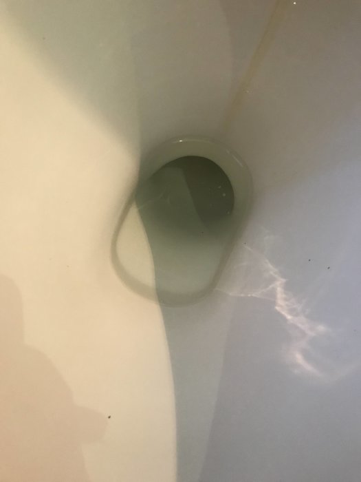 Närbild på en toalettstol efter backspolning med tydliga vattenlinjer och skuggor.