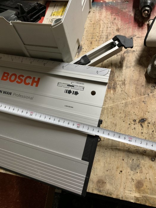 Ett måttband utdraget till 336 mm och en uppmätt del av en Bosch maskin, placerade på ett slitet arbetsbord.