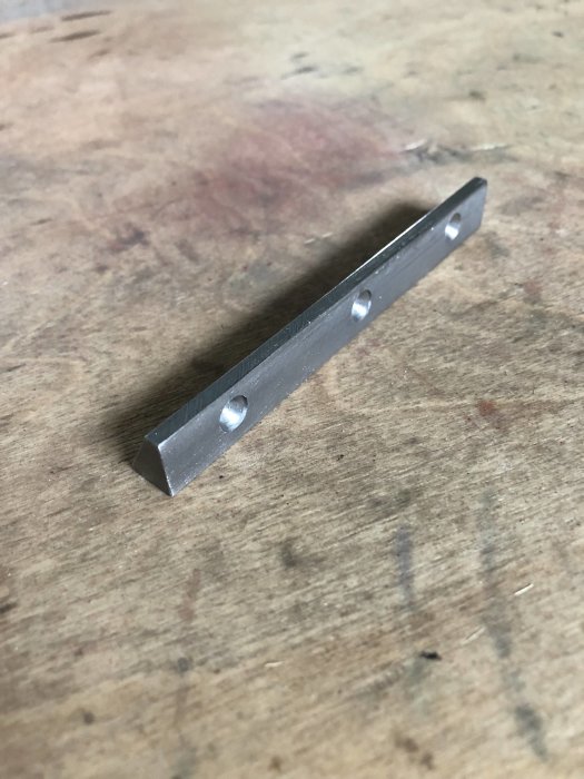 Metallkil med tre borade hål för justerskruvar på ett träbord.