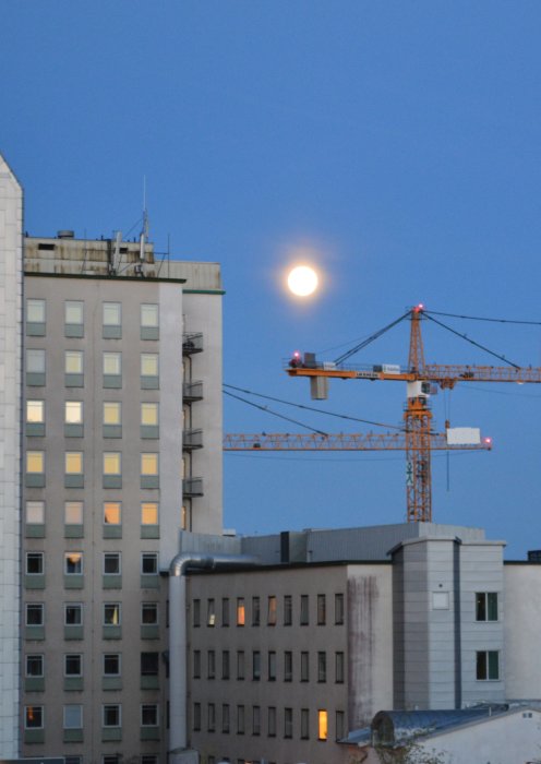 Fullmåne som lyser över byggnader och en kran på natten.