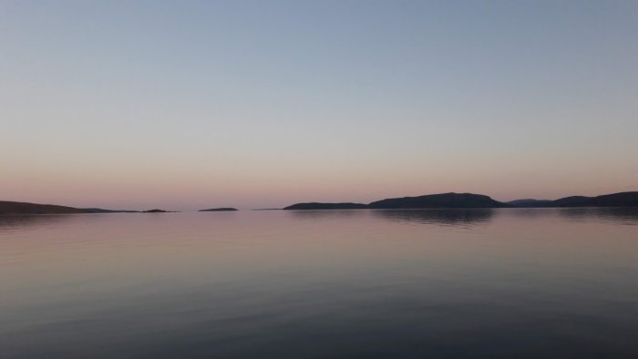 Stillasittande hav vid skymningen med silhuetter av kullar mot en pastellfärgad himmel.