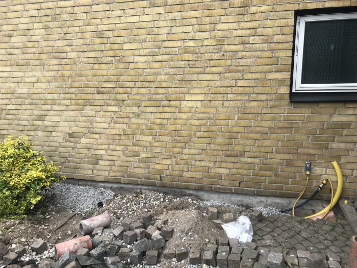 Husfasad med grusliknande mark framför, Gardena-koppling och gul PEM-slang nära trappsteg.