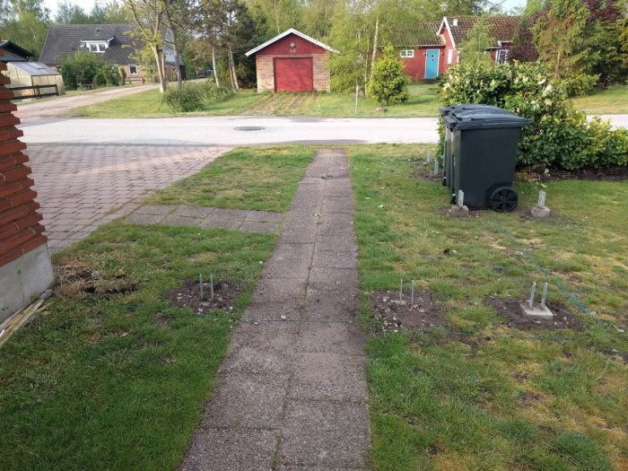 Trädgårdsgång med nyligen nergrävda plintar bredvid, och ett garage till vänster.