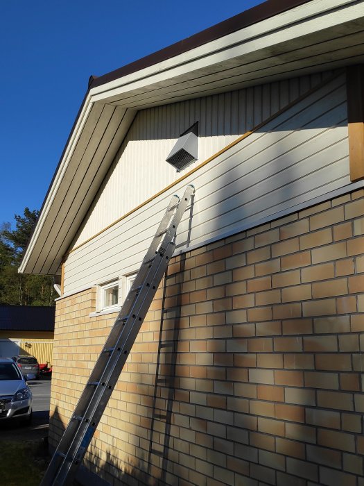 Nyinstallerad ventilation på en husgavel med en stege lutad mot väggen under en klarblå himmel.