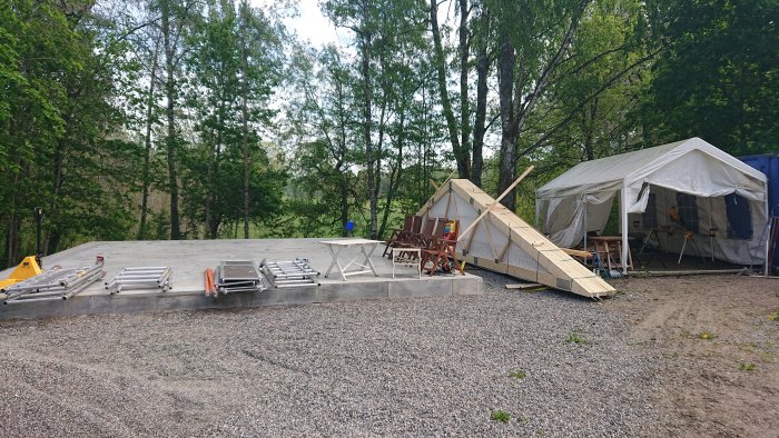 Betongplatta för garagebygge med färdigställda grunder, byggmaterial och arbetspaviljong på plats.