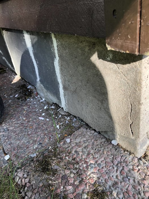 Skadad betonggrund till en byggnad med sprickor och flagning på ytan, bredvid stenbelagd mark.