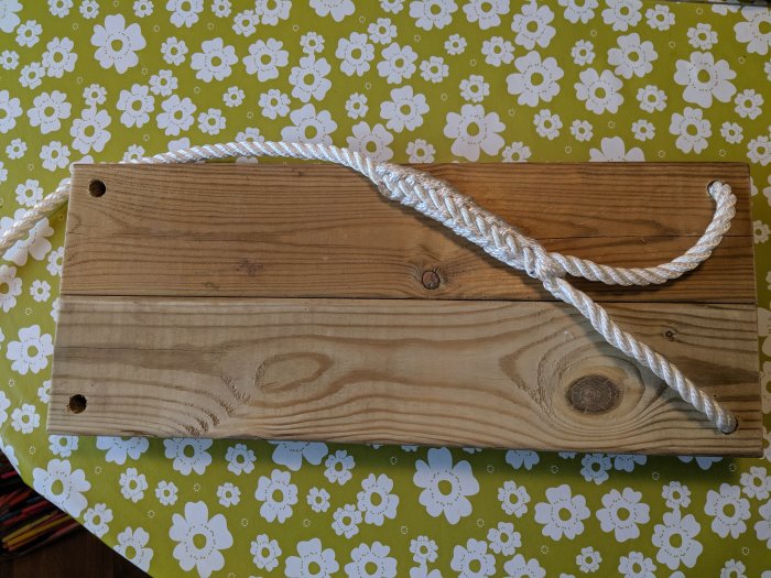 En träplanka med vitt rep slingrat över, på ett bord med blommigt tyg.