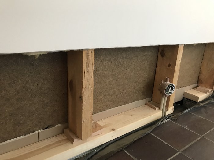 Delvis installerad rörledning med trästöd och isolering vid en vägg under renovering.