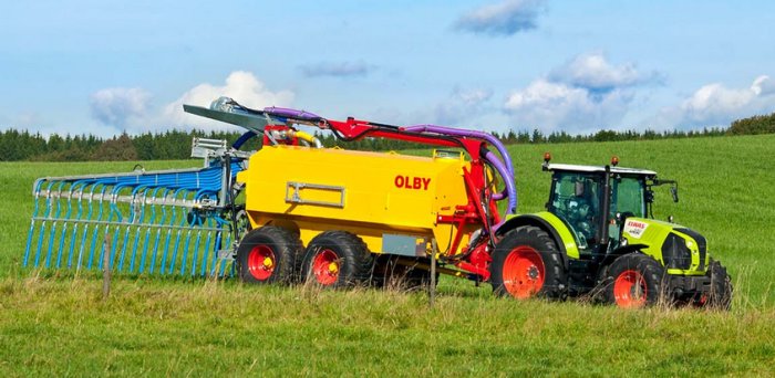 Traktor med gul gödseltank på en grön åkermark under dagtid.