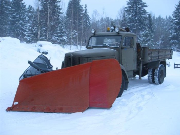 Gammal Scania lastbil med röd spetsplog i snöigt landskap.