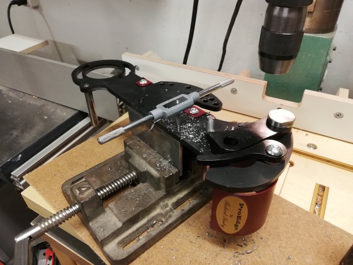Skruvstäd och borrpress används för att verkstadsarbete med svart metallstycke och träbitar.