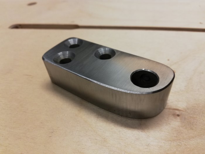 Metalldel som är tänkt att fästa en slipad axel för anpassning av slipjigg, visar hål för stoppskruvar och bearbetad yta.