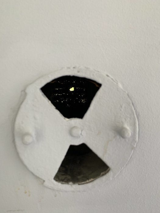 Gammal målad ventil i vägg med synlig mörk öppning och utsikt till utomhus genom vägg.